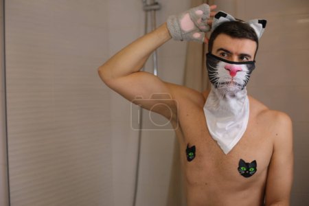 Téléchargez les photos : Portrait de beau jeune homme torse nu avec costume de chat devant le miroir dans la salle de bain - en image libre de droit