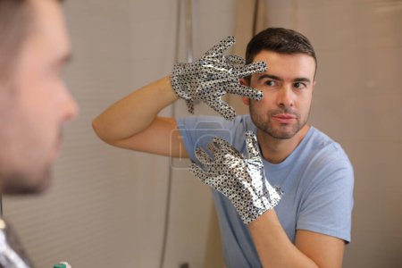 Photo for Portrait of handsome young man with silver glossy gloves in front of mirror in bathroom - Royalty Free Image