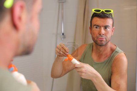 Téléchargez les photos : Portrait de beau jeune homme avec des coups de soleil devant le miroir dans la salle de bain - en image libre de droit