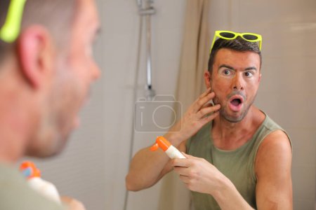 Téléchargez les photos : Portrait de beau jeune homme avec des coups de soleil devant le miroir dans la salle de bain - en image libre de droit