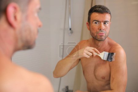 Téléchargez les photos : Portrait de beau jeune homme avec bronzant sur la peau devant le miroir dans la salle de bain - en image libre de droit