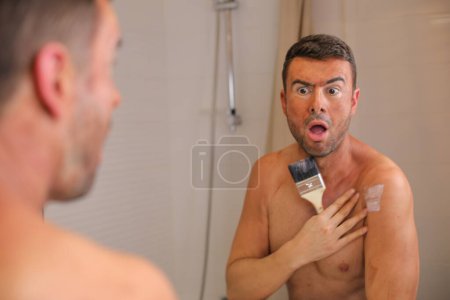 Téléchargez les photos : Portrait de beau jeune homme avec bronzant sur la peau devant le miroir dans la salle de bain - en image libre de droit
