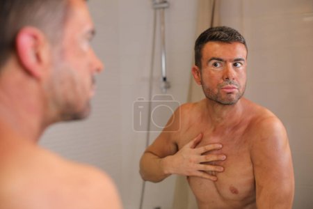 Photo for Portrait of handsome young man with bronzer on skin in front of mirror in bathroom - Royalty Free Image