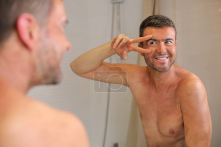Photo for Portrait of handsome young man with bronzer on skin in front of mirror in bathroom - Royalty Free Image