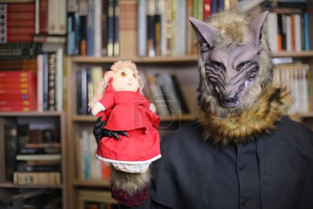 Photo for Close-up shot of person in wolf mask at home with red hood toy - Royalty Free Image