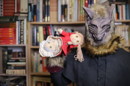 Téléchargez les photos : Gros plan de la personne dans le masque de loup à la maison avec un jouet capuche rouge - en image libre de droit