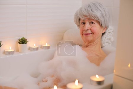 Téléchargez les photos : Portrait de femme âgée heureuse se détendre dans la baignoire avec des bulles de savon - en image libre de droit