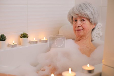 Téléchargez les photos : Portrait de femme âgée heureuse se détendre dans la baignoire avec des bulles de savon - en image libre de droit