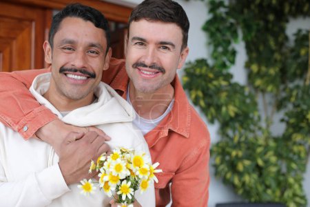 Téléchargez les photos : Jeune couple gay heureux de deux beaux hommes embrassant avec beau bouquet de fleurs de camomille - en image libre de droit