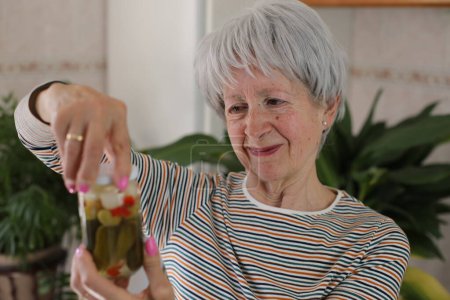 Photo for Portrait of mature grey haired woman holding jar of pickles at home - Royalty Free Image