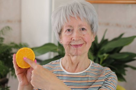 Foto de Retrato de mujer madura de pelo gris sosteniendo la mitad de naranja en casa - Imagen libre de derechos
