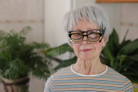 Photo for Portrait of funny mature grey haired woman with stack of eyeglasses at home - Royalty Free Image