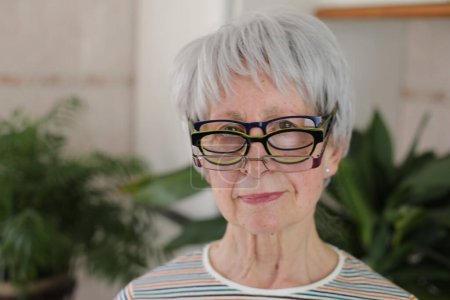 Foto de Retrato de mujer madura de pelo gris con pila de gafas en casa - Imagen libre de derechos