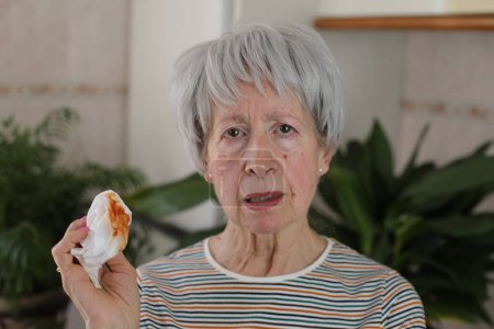 Téléchargez les photos : Portrait d'une femme mûre aux cheveux gris tenant une serviette avec du sang à la maison - en image libre de droit