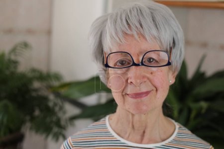 Téléchargez les photos : Portrait de femme mûre aux cheveux gris avec des lunettes à l'envers à la maison - en image libre de droit