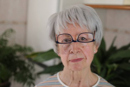 Téléchargez les photos : Portrait de femme mûre aux cheveux gris avec des lunettes à l'envers sur le visage à la maison - en image libre de droit