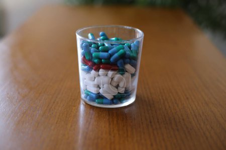 Téléchargez les photos : Plan rapproché de verre rempli de diverses pilules et médicaments sur une table en bois - en image libre de droit