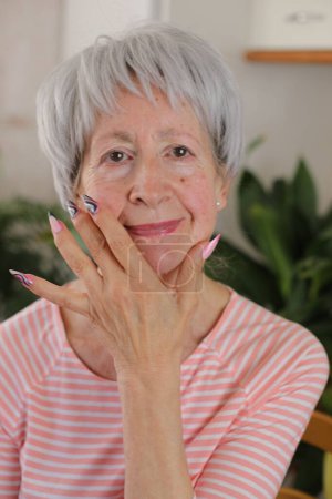 Téléchargez les photos : Portrait de heureuse femme mûre aux cheveux gris avec des ongles colorés à la maison - en image libre de droit