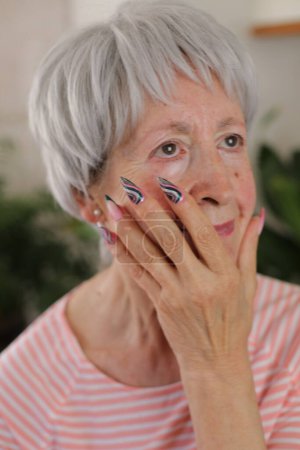Téléchargez les photos : Portrait de belle femme mature aux cheveux gris avec des ongles colorés à la maison - en image libre de droit