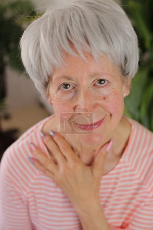 Foto de Retrato de mujer madura de pelo gris con uñas de colores en casa - Imagen libre de derechos