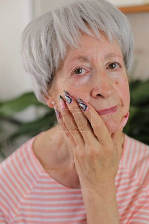 Téléchargez les photos : Portrait de femme mature aux cheveux gris avec des ongles colorés à la maison - en image libre de droit