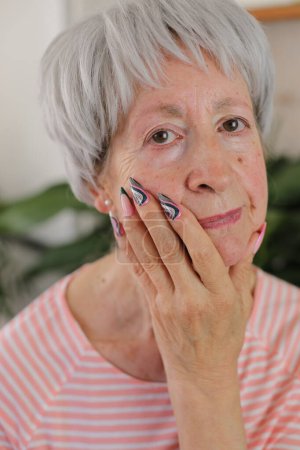 Téléchargez les photos : Portrait de femme mature aux cheveux gris avec des ongles colorés à la maison - en image libre de droit