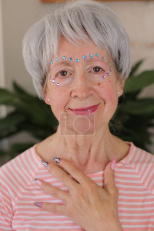 Téléchargez les photos : Portrait de femme mature aux cheveux gris avec des gemmes brillantes sur le visage et des ongles peints à la maison - en image libre de droit