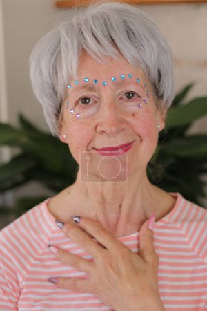 Photo for Portrait of mature grey haired woman with glossy gems on face and painted nails at home - Royalty Free Image