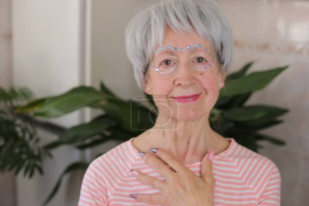 Photo for Portrait of mature grey haired woman with glossy gems on face and painted nails at home - Royalty Free Image