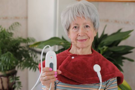 Femme âgée avec douleur au cou en utilisant un coussin chauffant électrique