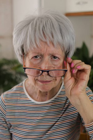 Mujer mayor entrecerrando los ojos y bajando las gafas