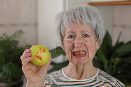 Mujer mayor con encías sangrientas después de morder una manzana