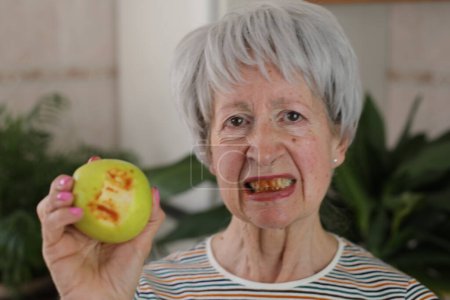 Mujer mayor con encías sangrientas después de morder una manzana