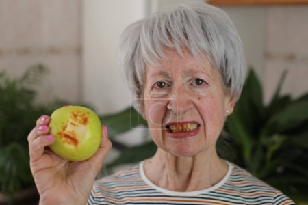Téléchargez les photos : Femme âgée avec des gencives sanglantes après avoir mordu une pomme - en image libre de droit