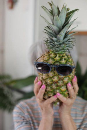 Photo for Senior woman holding a pineapple with sunglasses. - Royalty Free Image
