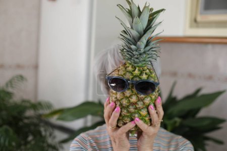 Photo for Senior woman holding a pineapple with sunglasses. - Royalty Free Image
