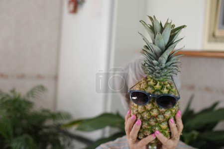 Foto de Mujer mayor sosteniendo una piña con gafas de sol. - Imagen libre de derechos