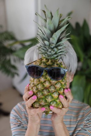 Foto de Mujer mayor sosteniendo una piña con gafas de sol. - Imagen libre de derechos