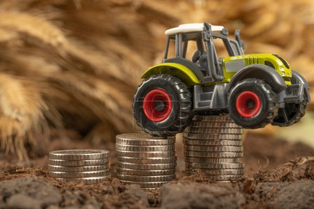 Téléchargez les photos : Tracteur avec de l'argent sur le fond d'épillets de blé. Exportations de céréales et d'agriculture. Hausse des prix des produits agricoles - en image libre de droit