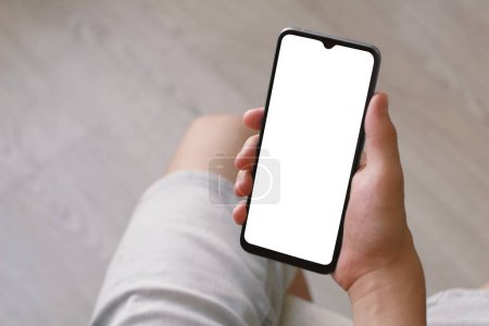 Photo for A teenager holds a smartphone with one hand. Phone with white screen on defocused light background. There is a work path in the file. - Royalty Free Image