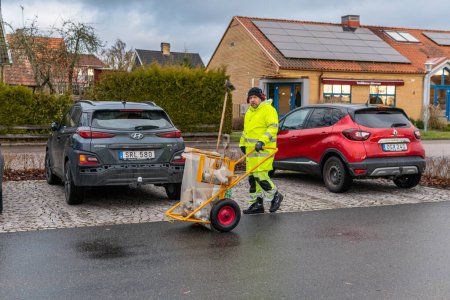 Photo for Sweden, Knislinge  January 3, 2023: A man in uniform picking up rubbish, cleaning up streets. Scavenger, dustman, garbage collector, ashman. - Royalty Free Image
