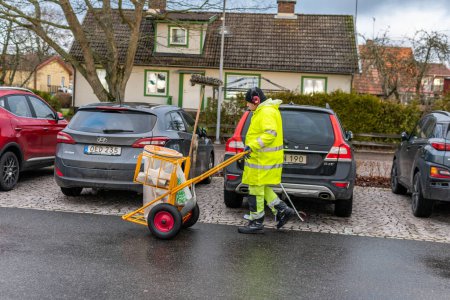 Photo for Sweden, Knislinge  January 3, 2023: A man in uniform picking up rubbish, cleaning up streets. Scavenger, dustman, garbage collector, ashman. - Royalty Free Image