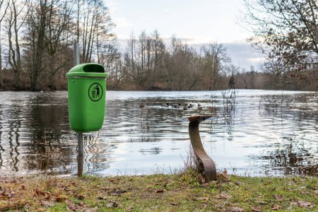 Foto de Un cubo de basura verde cerca de un lago, inundado y no se puede llegar. Símbolo del ser humano y la naturaleza. - Imagen libre de derechos