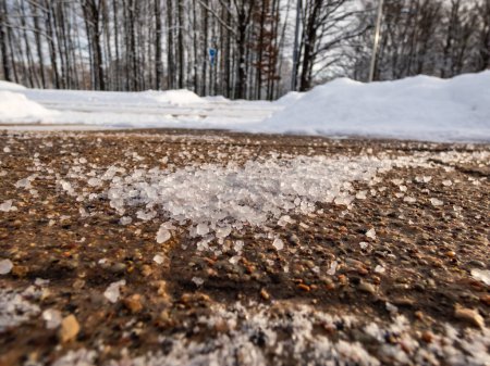 Téléchargez les photos : Saler les grains sur le trottoir glacé en hiver. Appliquer du sel pour garder les routes dégagées et les gens en sécurité par temps hivernal contre la glace ou la neige. Macro vue des grains de sel avec des paysages d'hiver blanc dans le bacground - en image libre de droit