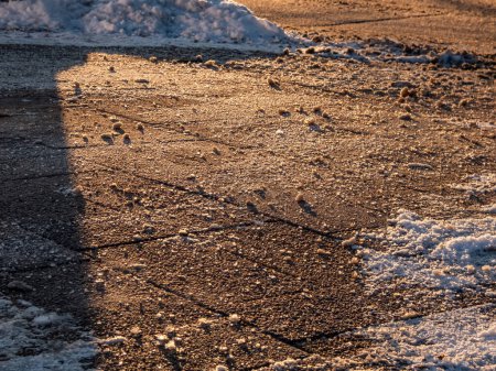 Téléchargez les photos : Saler les grains sur le trottoir glacé en hiver. Appliquer du sel pour garder la route libre et les gens en sécurité par temps hivernal contre la glace ou la neige. Vue macro des grains de sel au soleil en hiver - en image libre de droit