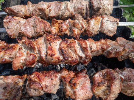 Photo for Cooked meat on metal skewers - juicy red meat grilling and cooking on coals on a grill. Herbed and seasoned cubes of meat with brown crust. Picnic and grilling meat - Royalty Free Image