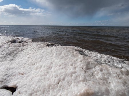 Seestück, das die Landschaft der Ostsee und des Strandes mit Eis- und Schneeformationen am Ufer im hellen Sonnenlicht darstellt. Gefrorene Eisblöcke und Meerwasser im Winter