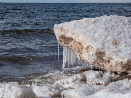 Nahaufnahme der Schnee-, Eis- und Eiszapfenformationen im Ostseewasser am Ufer bei gleißendem Sonnenlicht. Gefrorene Eisblöcke und Meerwasser im Winter