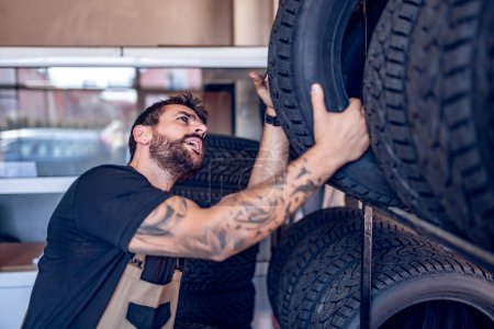 Photo for Mechanic holding a tire at the repair garage. Replacement of winter and summer tires. - Royalty Free Image