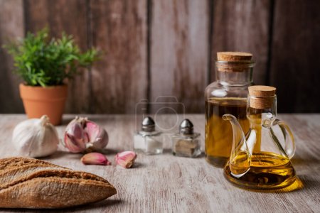 Natives Olivenöl extra in einer Ölkanne und in einer kleinen Flasche auf einem Holztisch .